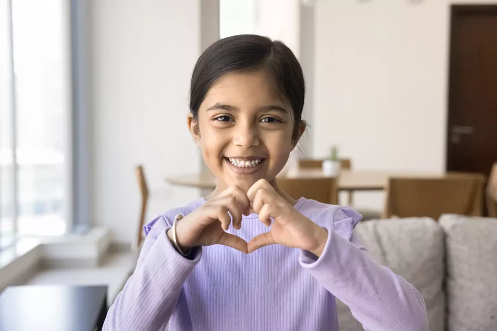 A young girl is smiling while making a love symbol with her hands