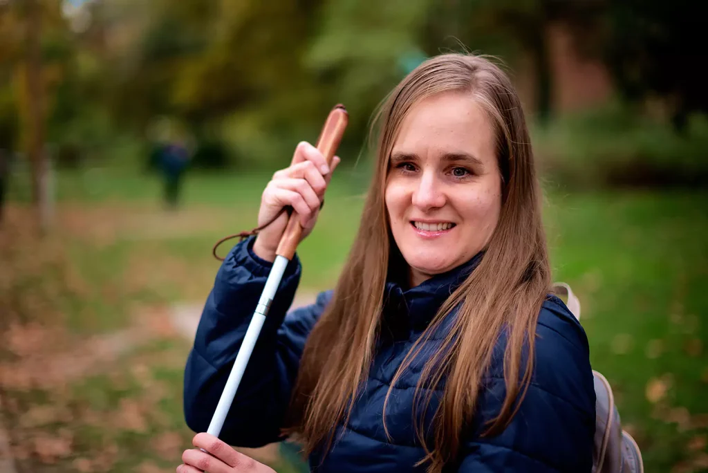 A blind woman is sitting at a public park. She is smiling and enjoying herself.