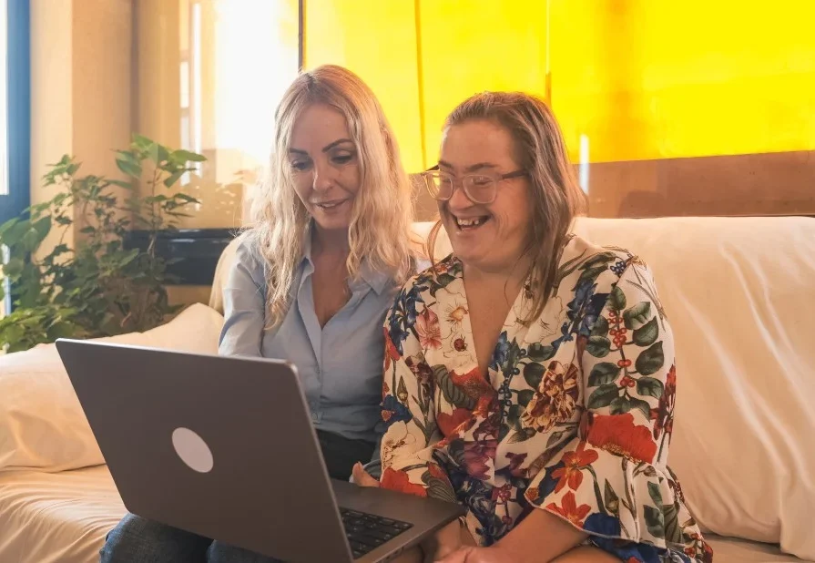 A support worker is showing a woman with down syndrome something on her laptop